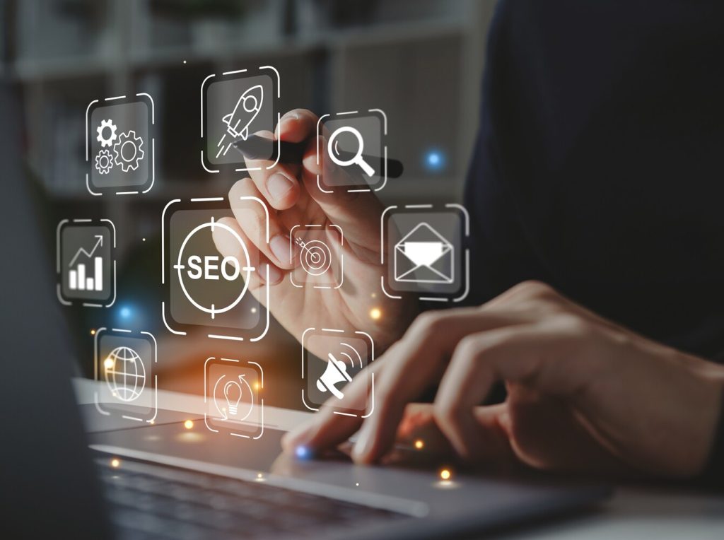 Hand of businessman holding a pen pointing to SEO Search Engine Optimization on laptop screen.