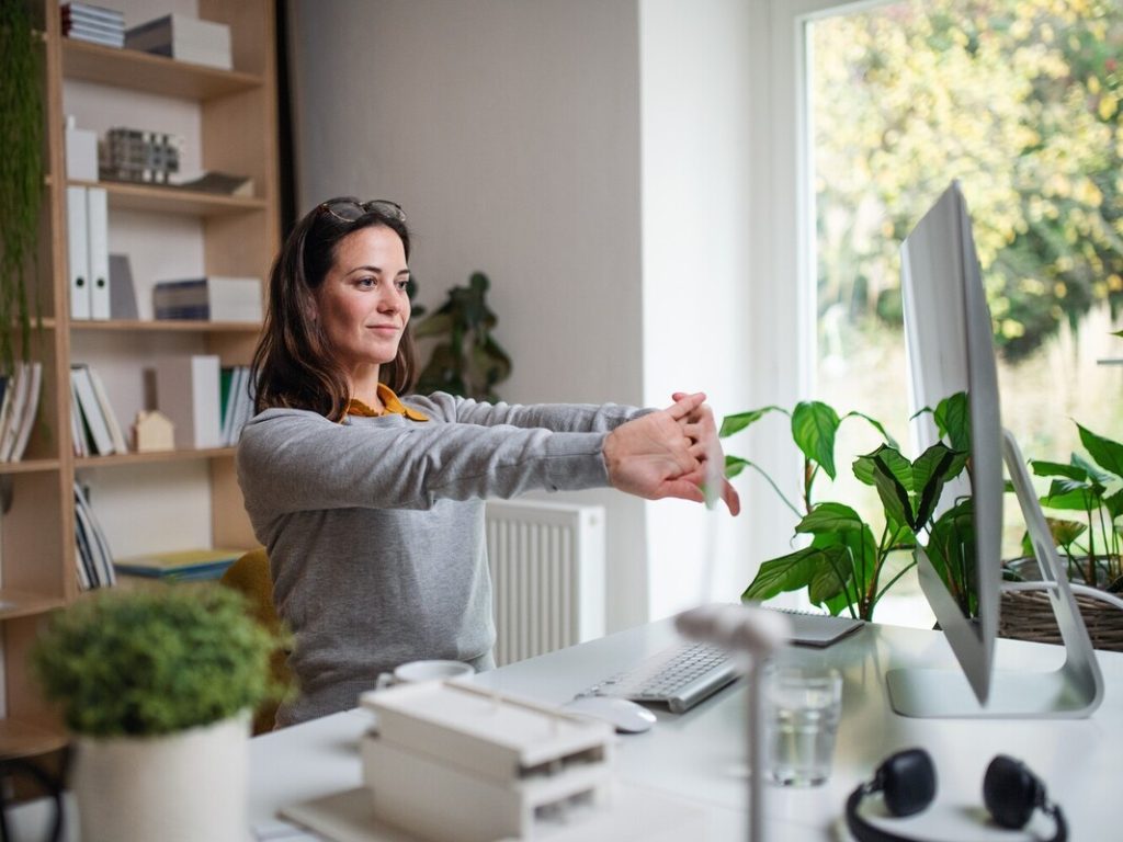 Businesswoman sitting indoors in office, stretching.