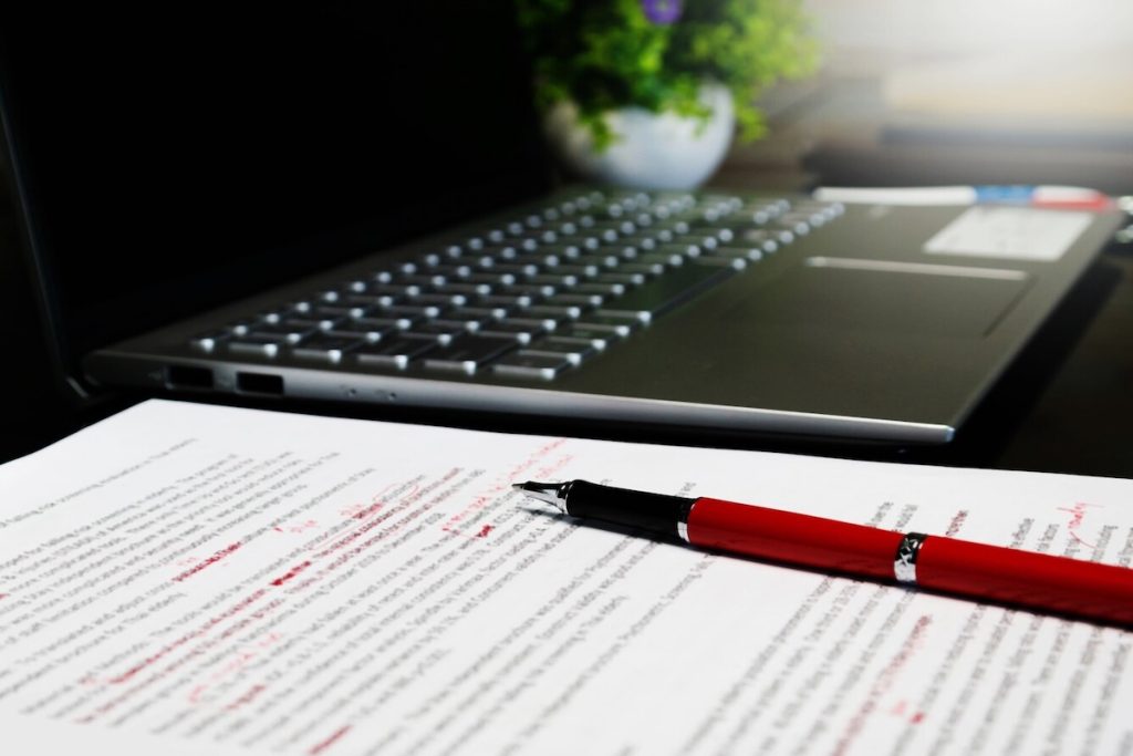red fountain pen resting on marked paper next to idle laptop