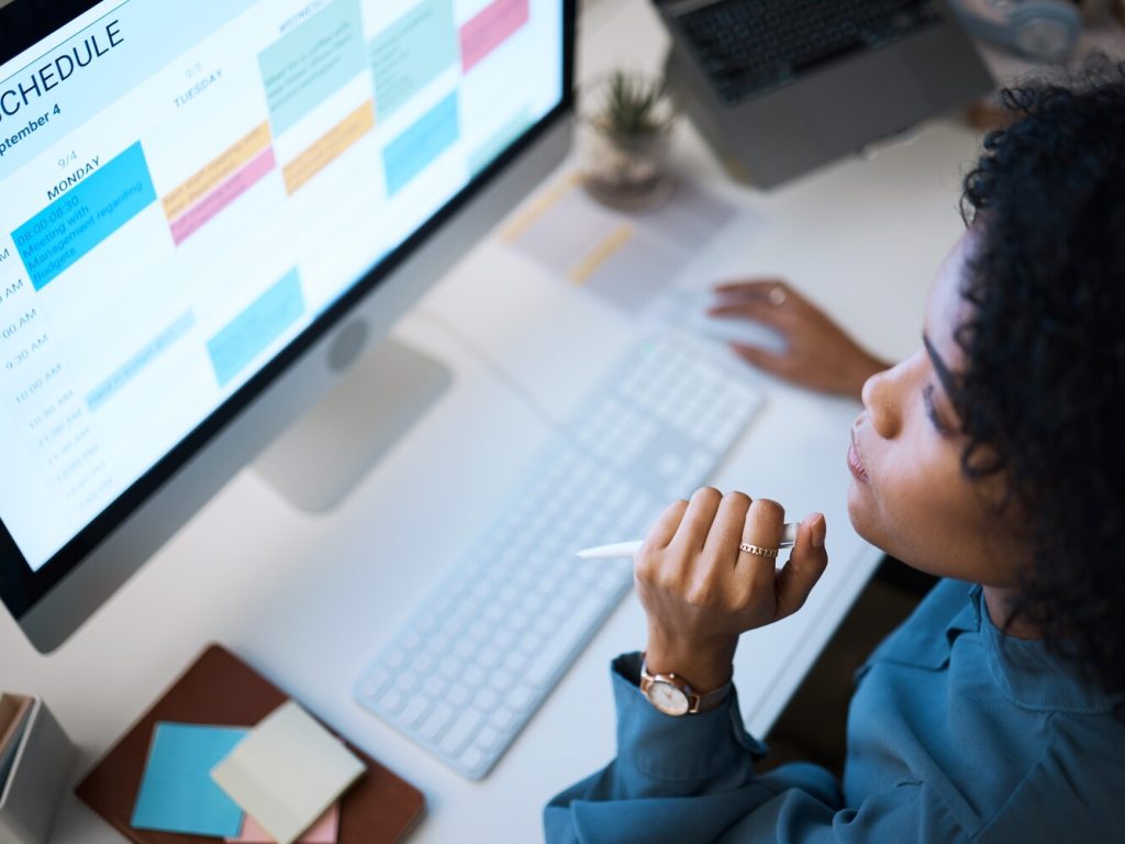 Woman with computer, thinking and checking schedule, agenda and reminder for office administration. Online calendar, planner and girl at desk planning spreadsheet for time management with high angle.